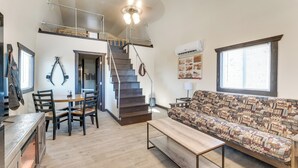 Amplia sala de estar con piso de madera, un sofá con funda estampada, una mesa de comedor con sillas, una escalera y una chimenea.