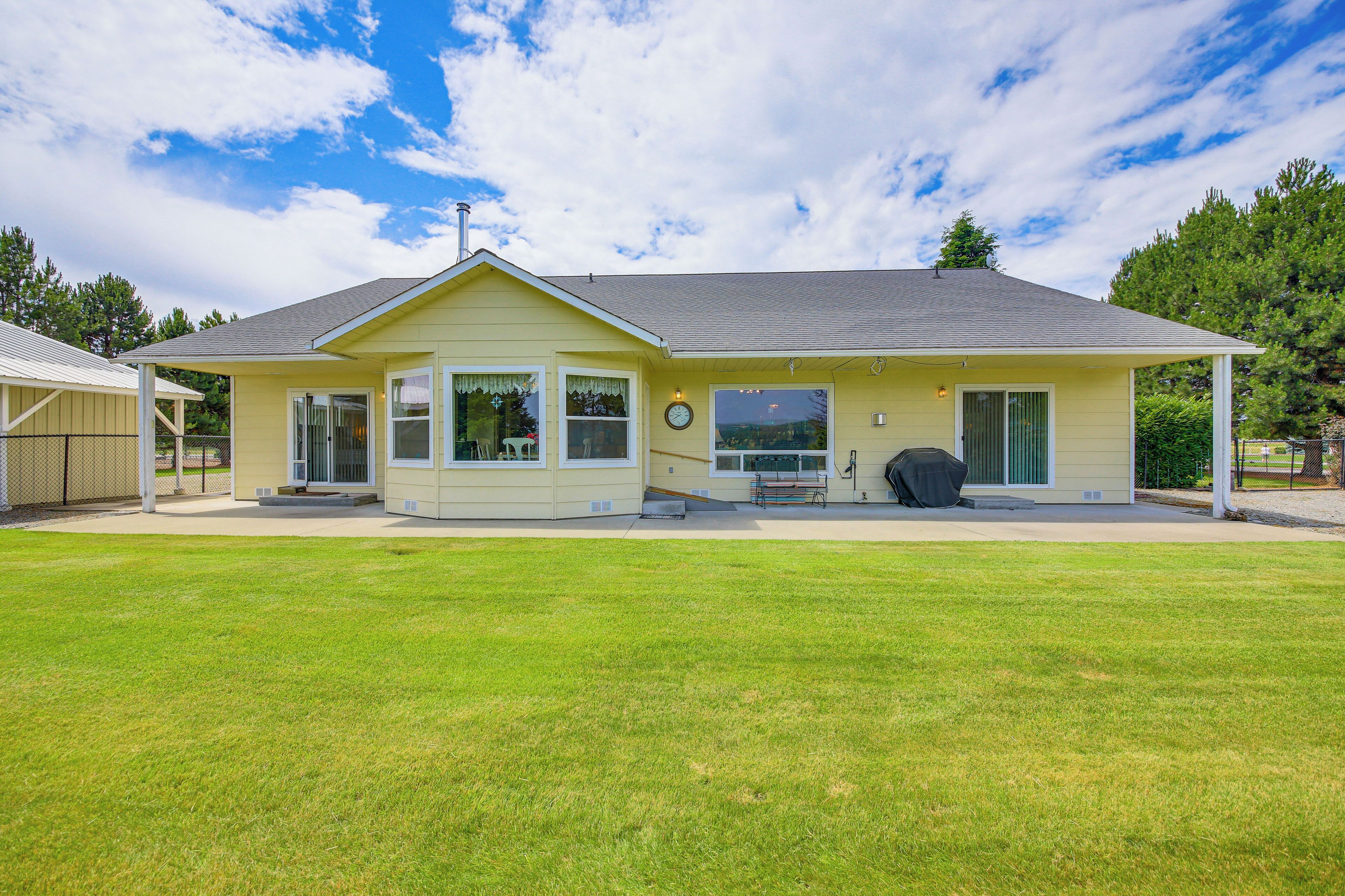 A single-story house with a covered patio, a lawn, and a view of the surrounding area.