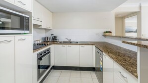 Una cocina moderna con gabinetes blancos, encimera de granito, horno empotrado y microondas.