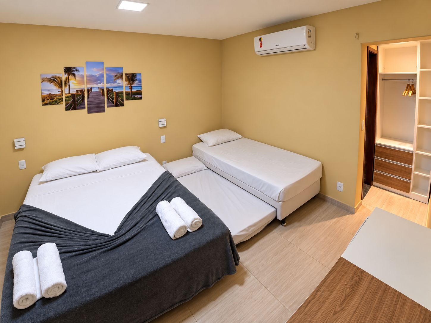 Habitación de hotel con dos camas, un armario, aire acondicionado de pared y varias fotografías con motivos playeros.