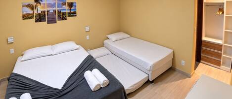 A hotel room with two beds, a wardrobe, a wall-mounted air conditioner, and a series of beach-themed pictures.