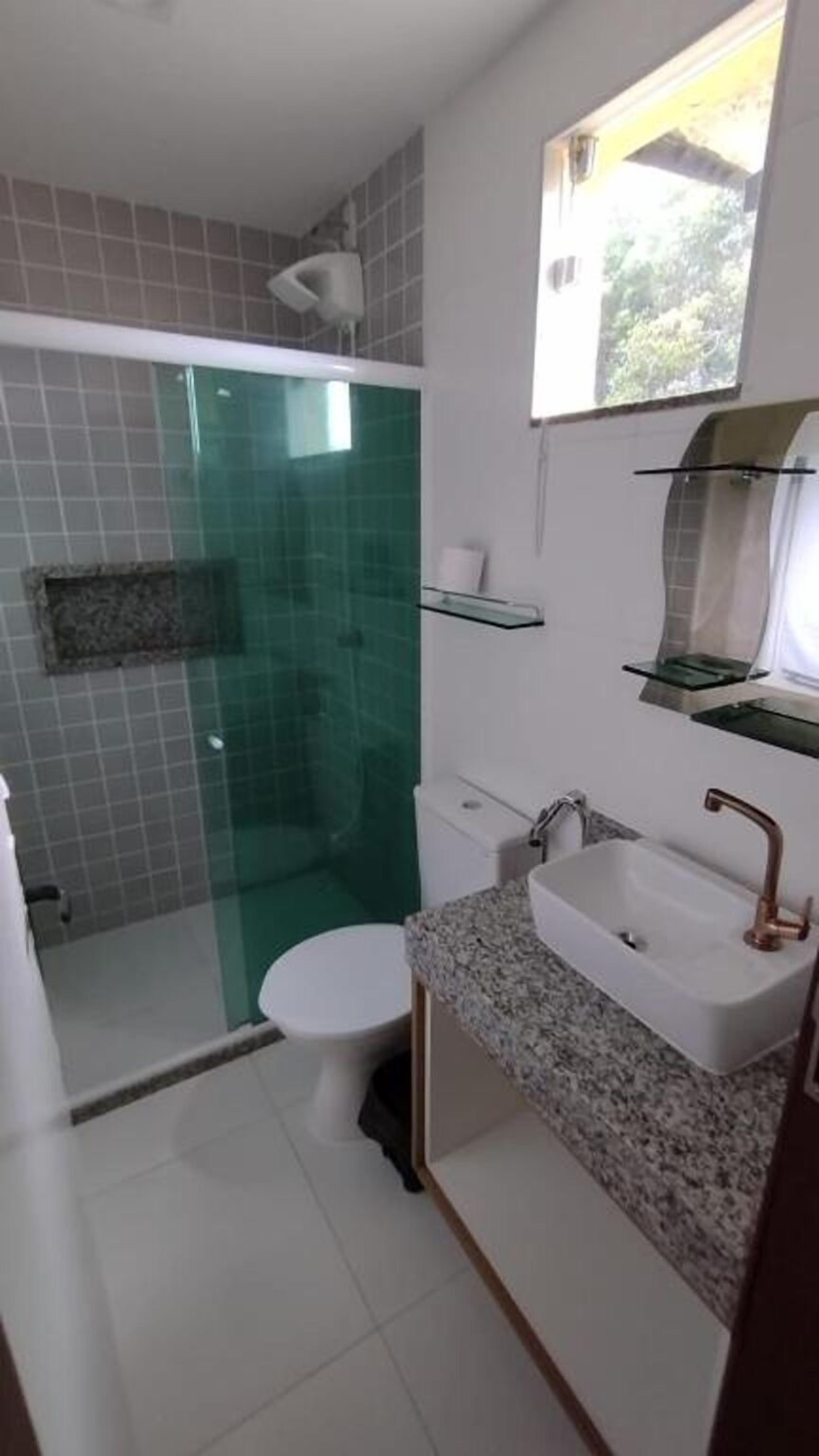 A bathroom with a glass shower enclosure, a toilet, a sink with a mirror, and shelves above the sink.