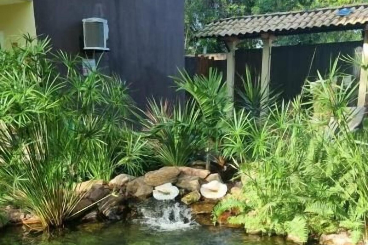 Piscina cristalina con dos personas nadando, rodeada de abundante vegetación y una pequeña cascada.