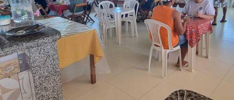 A covered dining area with tables and chairs, large windows, and a tiled floor.