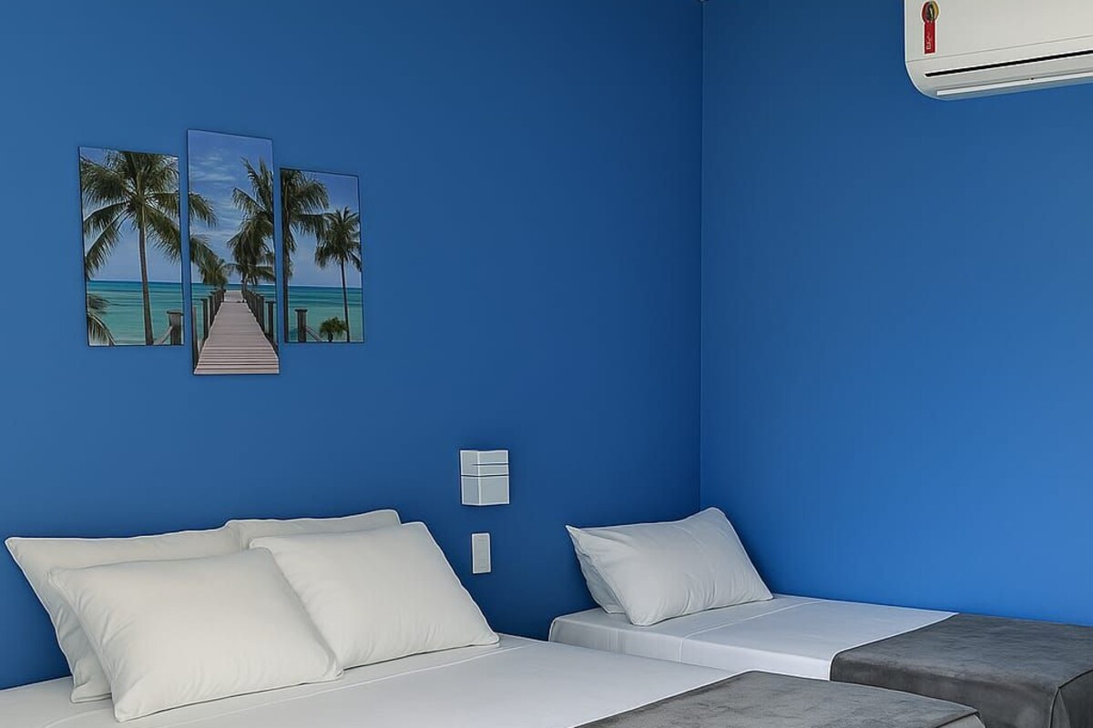 Una habitación con dos camas, una pared azul y una obra de arte con temática de playa.