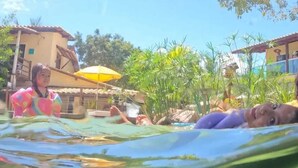 Zona de piscina con agua cristalina, rodeada de follaje y edificios.