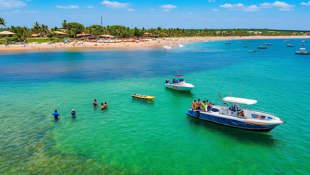 Una playa tropical con aguas turquesas cristalinas, varias embarcaciones y una orilla arenosa bordeada de palmeras.