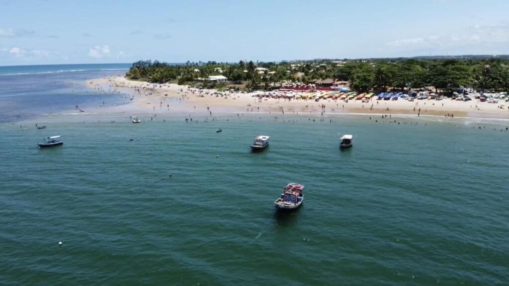 A beach with boats on the water and a sandy shore with umbrellas.