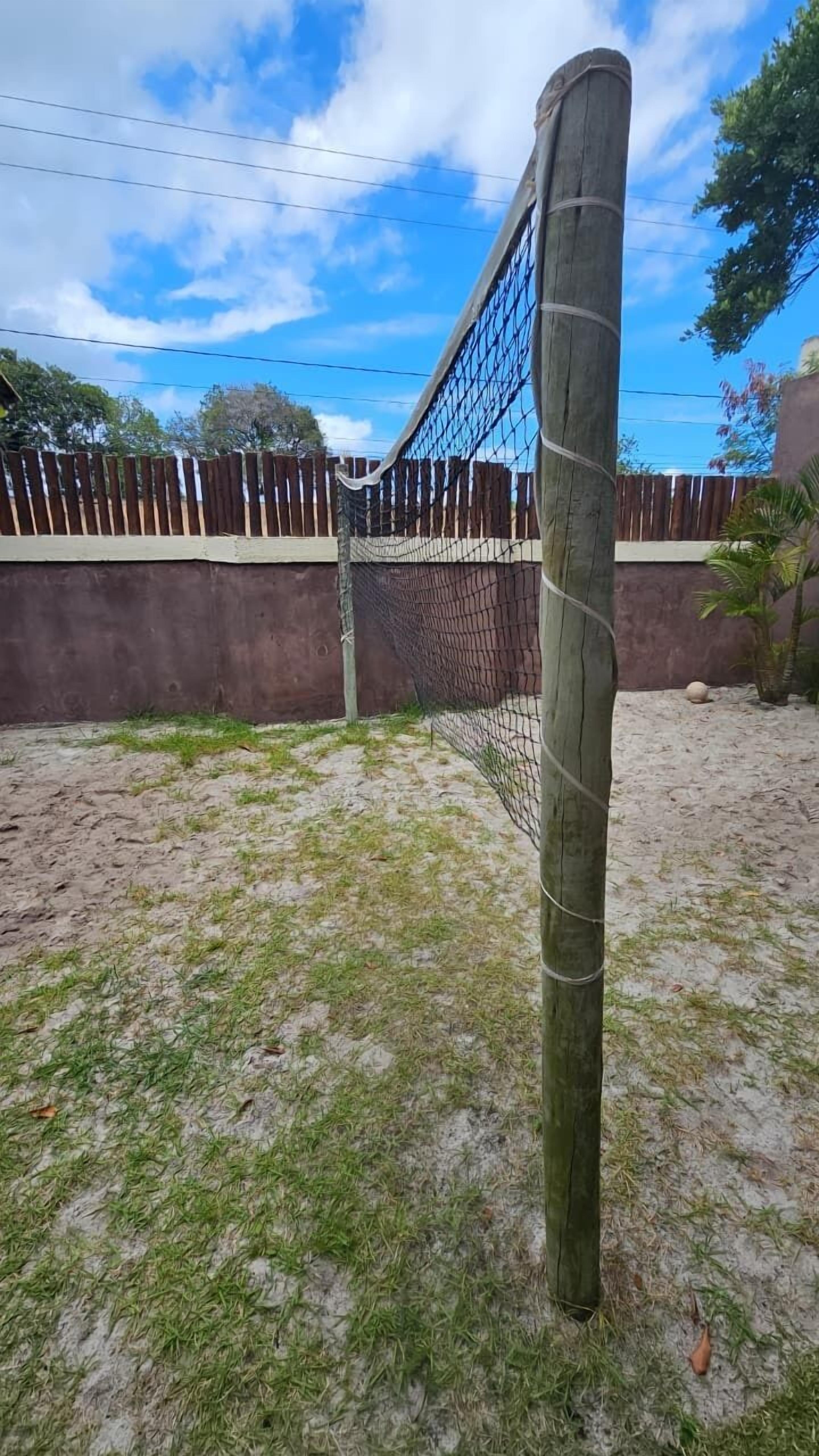 Un filet de volley-ball, maintenu par un poteau en bois, installé sur une surface sablonneuse où l’herbe est clairsemée.