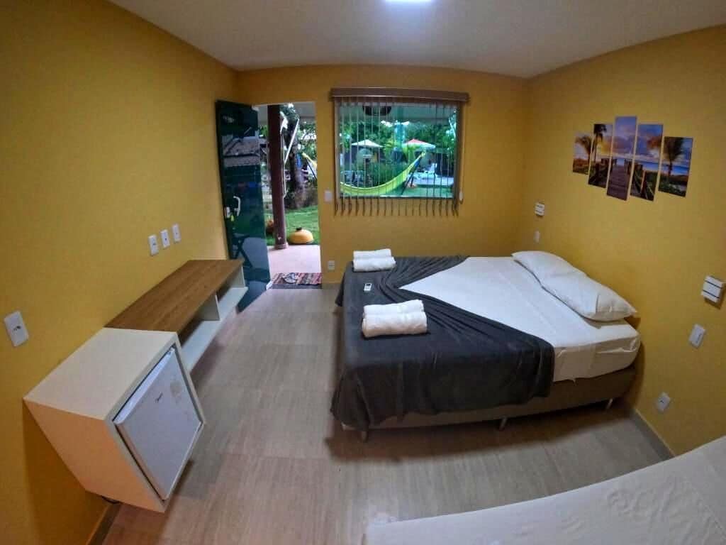 A small, single-bed room with a desk, a window with a view of a garden, and a wall with pictures.