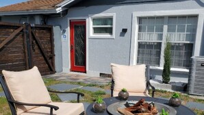 Eine Terrasse mit rundem Tisch, zwei Stühlen, einer kleinen Feuerstelle und einer roten Tür.