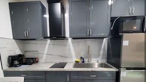 Eine moderne Küche mit dunkelgrauen Schränken, einem Edelstahlkühlschrank, einer Mikrowelle und einem Gasherd. Es gibt ein Spülbecken mit einem Wasserhahn sowie eine Kaffeemaschine auf der Arbeitsplatte.
