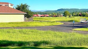 Paisagem rural com estrada pavimentada, campos verdes e edifícios com telhados vermelhos ao fundo.