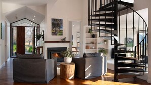 A modern living room with a fireplace, two grey sofas, a wooden coffee table, and a black spiral staircase. - The Falls at Lake Werona (Werona)