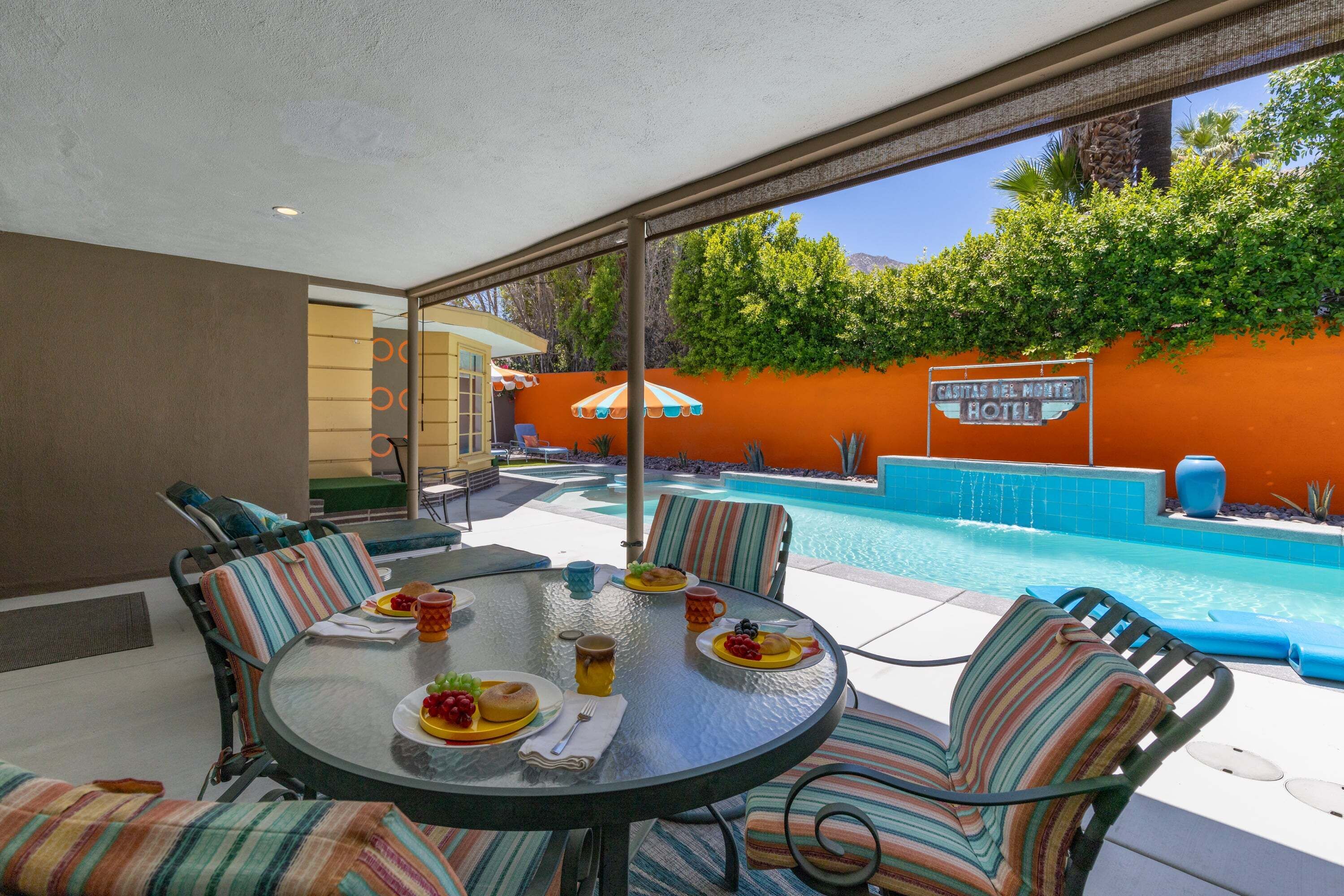 Zona de comedor junto a la piscina con una mesa, sillas y vistas a la piscina y al cartel del hotel.