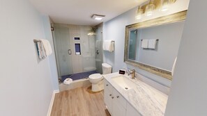 A modern bathroom with a glass shower enclosure, a white toilet, a marble sink, and a large mirror.