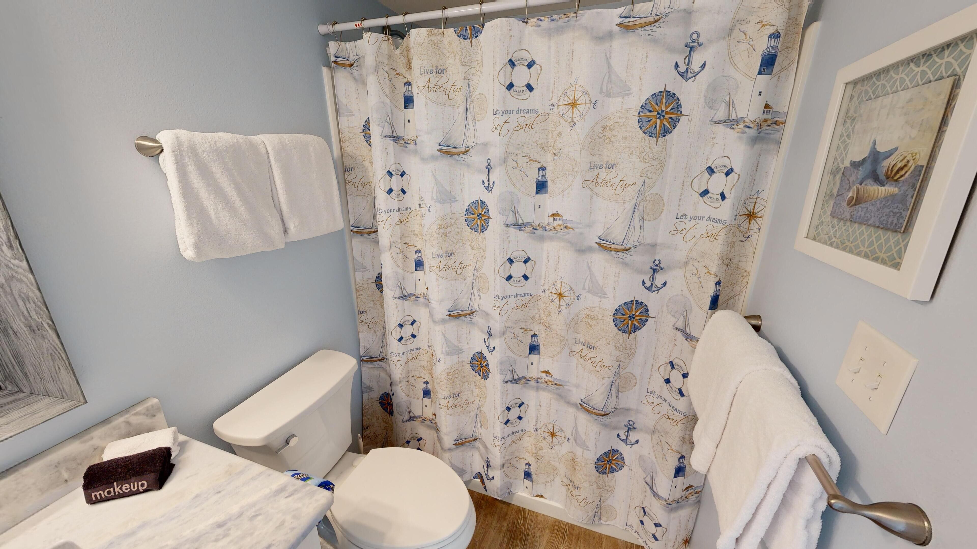 Une salle de bain avec un rideau de douche à motifs nautiques, des toilettes, un lavabo avec une serviette pour se maquiller et un porte-serviettes.