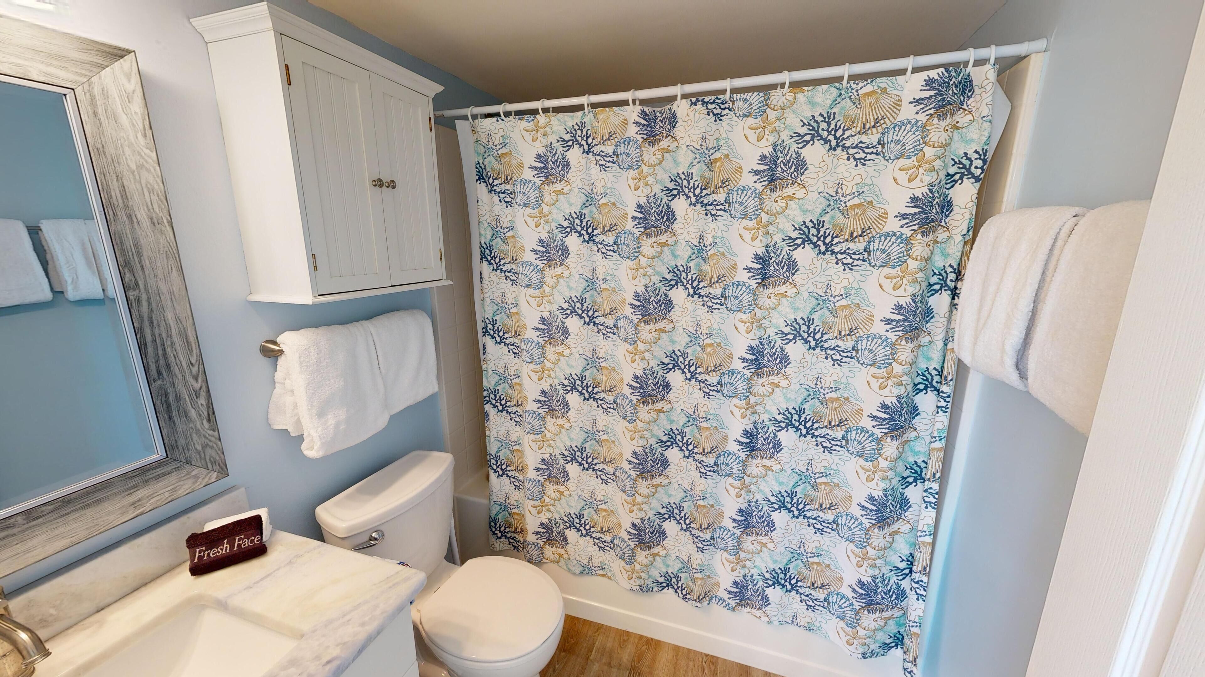 Et badeværelse med toilet, vask og brusebad med et marinelivsmønster.