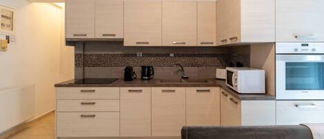 A modern kitchen with light wood cabinets, a black countertop, a microwave, and a built-in oven.