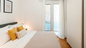Une chambre à coucher comprenant un lit, une table de chevet, un tableau encadré et une porte-fenêtre coulissante donnant sur un balcon.