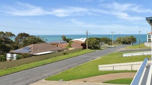 A residential street with houses, a clear sky, and a view of the ocean.
