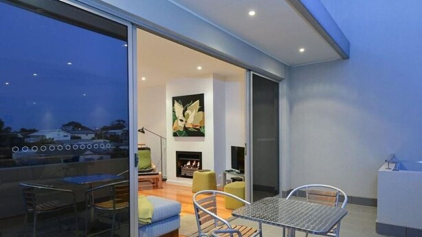 A modern living room with a fireplace, a dining area with metal chairs, and a glass sliding door leading to an outdoor space.