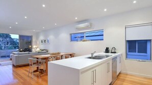 A modern kitchen with a central island, a dining area with a table and chairs, and a living area with a sofa and a TV.