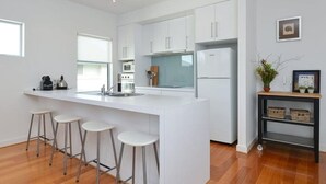 A modern kitchen with white cabinetry, a central island with stools, a built-in oven, and a refrigerator.