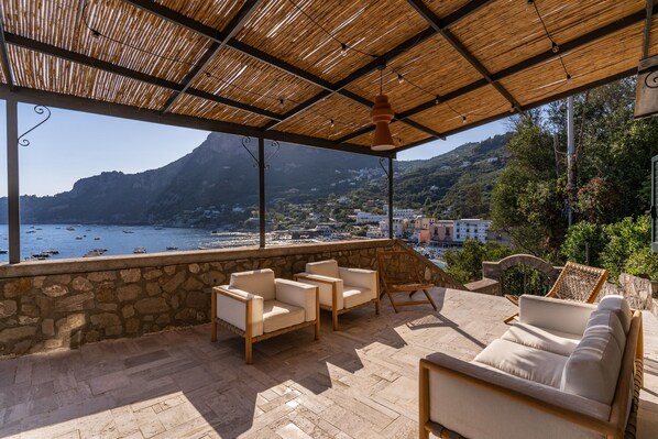 A covered outdoor seating area with stone walls, wicker furniture, and a view of the sea and mountains. - Villa Neranite in Citt Metropolitana di Napoli (Massa Lubrense)