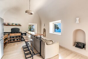 Une cuisine spacieuse avec une table en bois, des tabourets de bar et une vue sur la mer par la fenêtre.