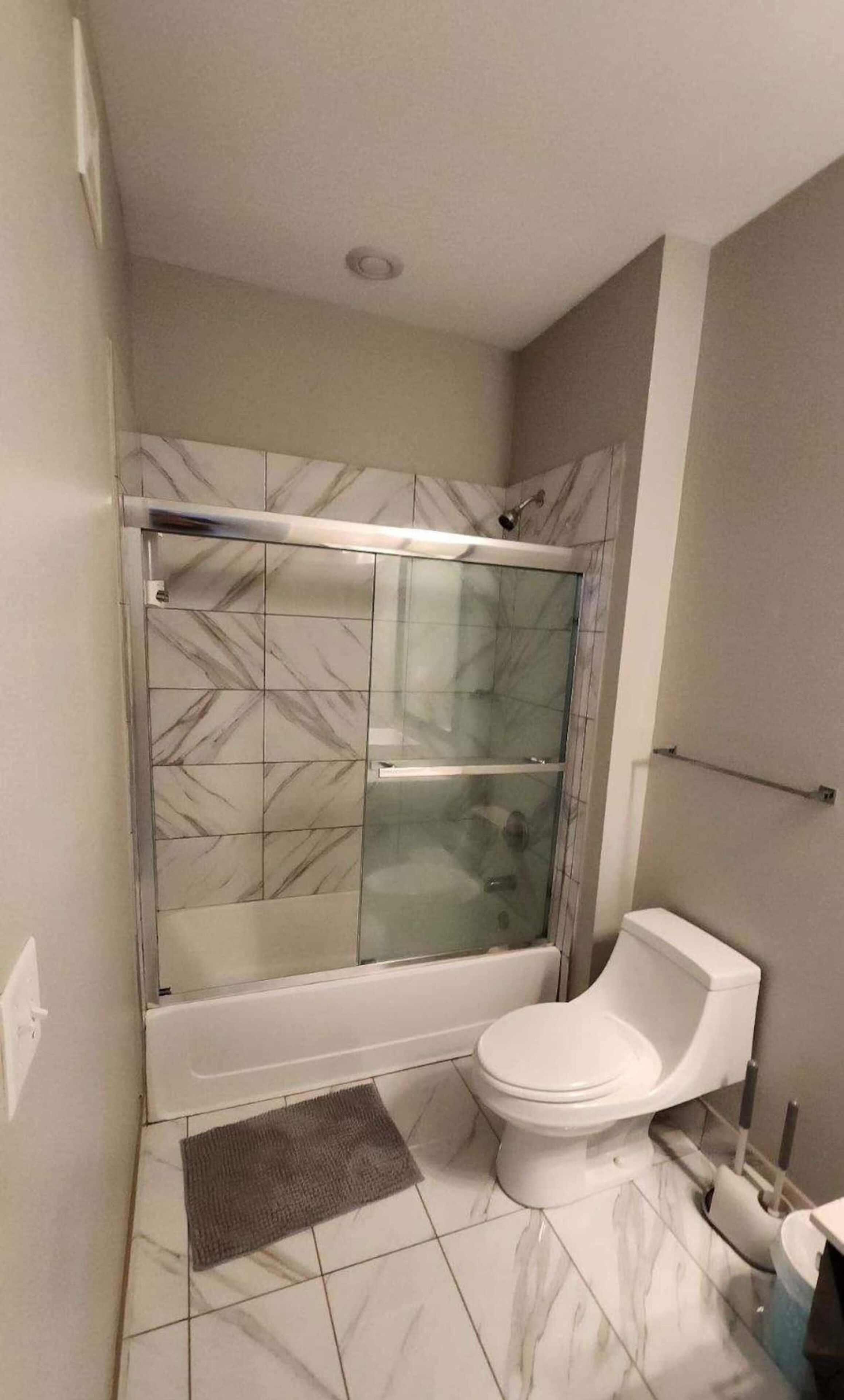 Un baño con ducha envuelta en vidrio, inodoro y suelo estampado con diseño de mármol.