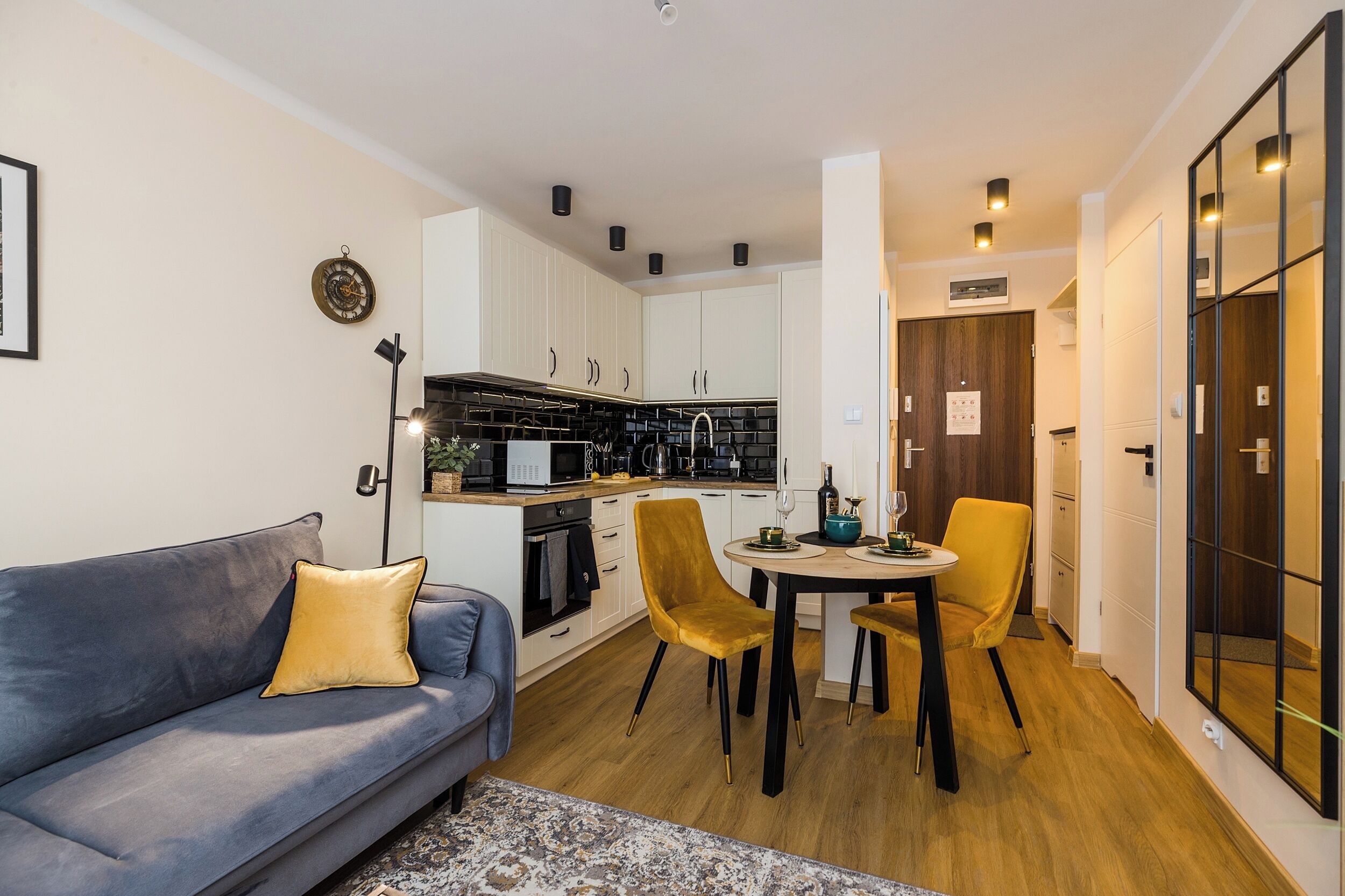 Een moderne keuken met witte kasten, een zwarte spatwand en een eethoek met gele stoelen.