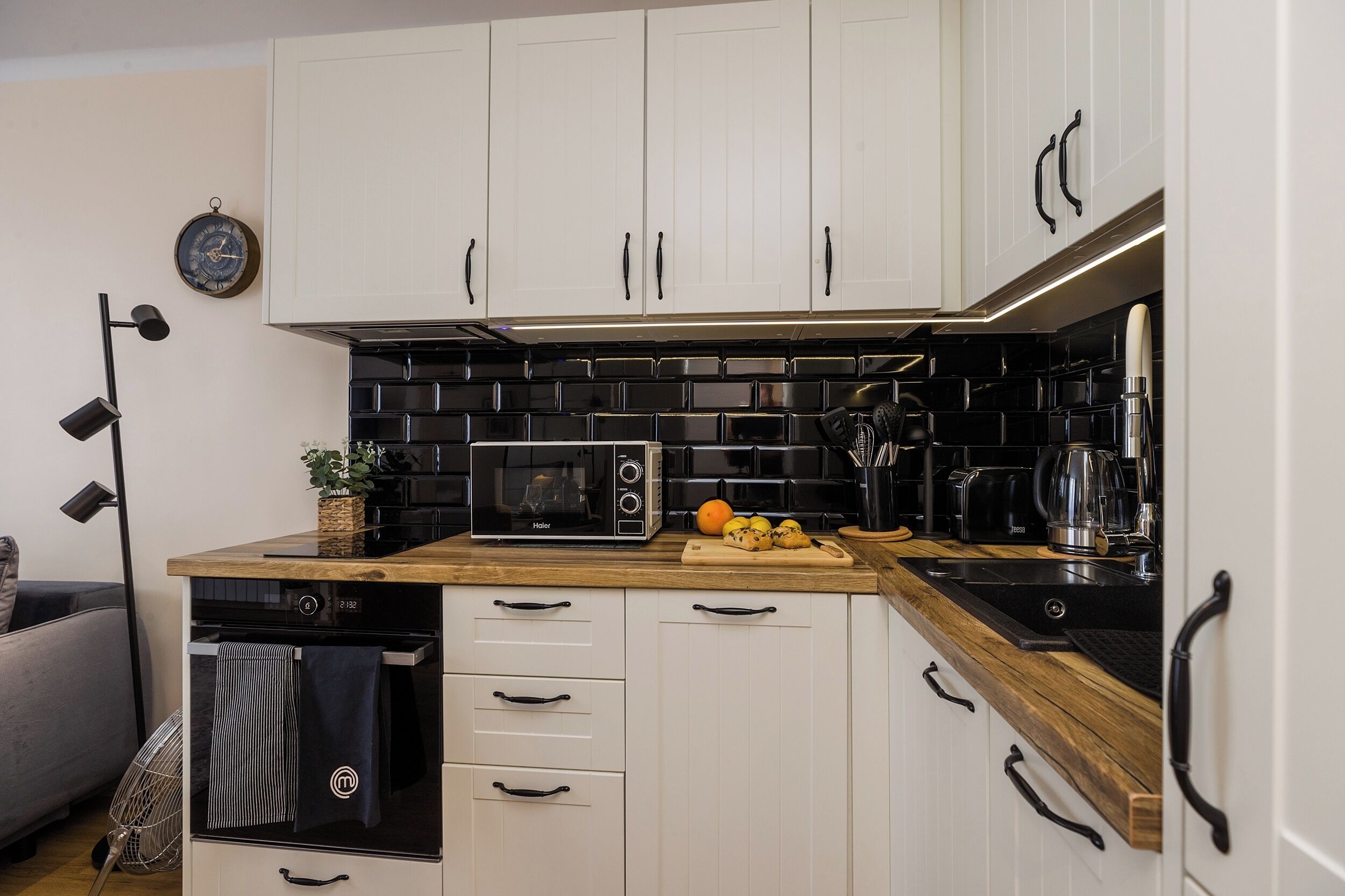 A modern kitchen with white cabinets, a black tiled backsplash, and a built-in microwave.