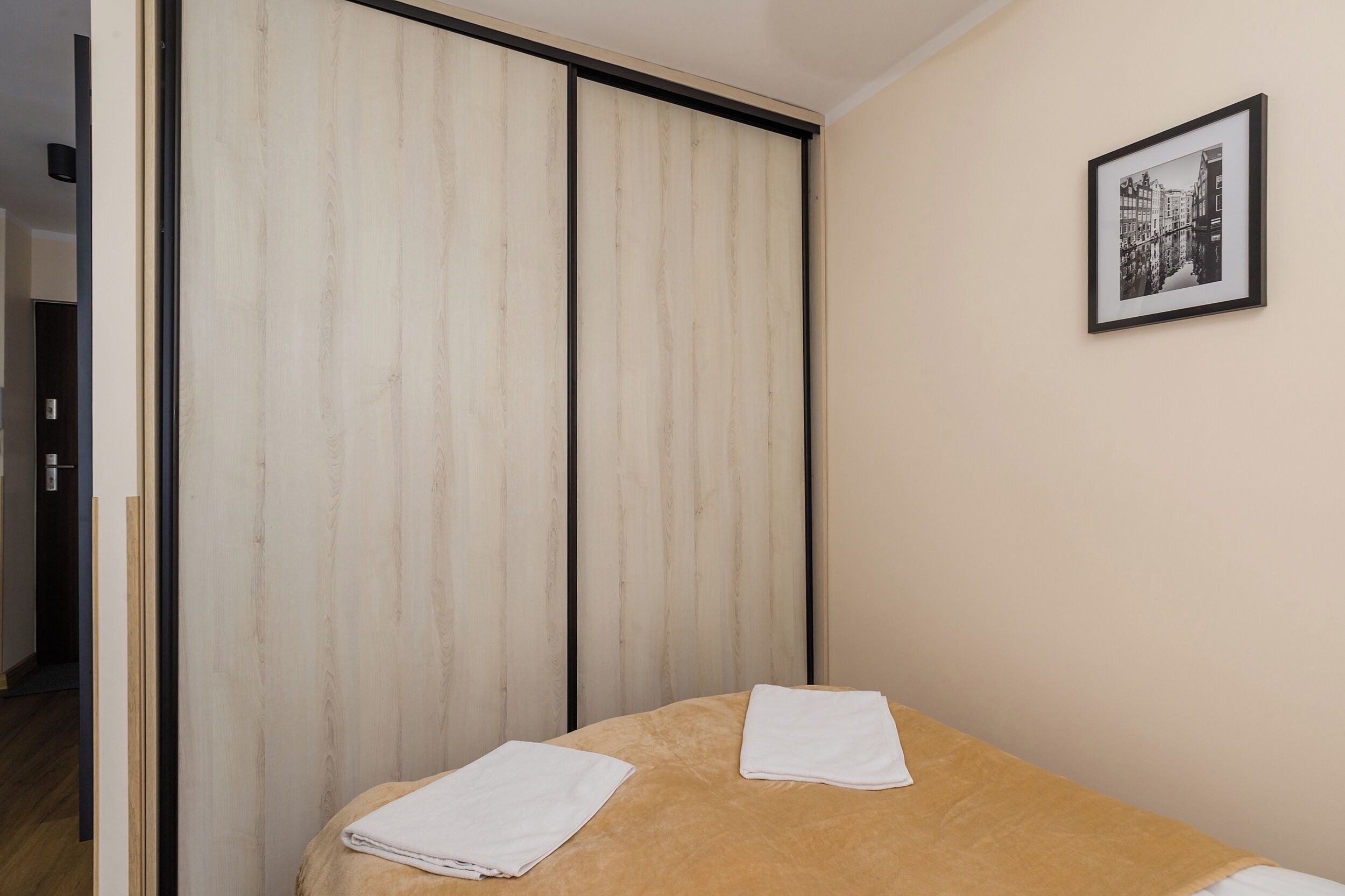 A bedroom with a bed, two towels, a wooden wardrobe, and a framed picture on the wall.