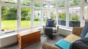 A conservatory with large windows, a wooden bench, and a wicker sofa with cushions. - Little Buckley Peaceful Family Retreat Nr Sidmouth (Sidbury)