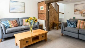 A living room with two grey sofas, colorful cushions, a wooden coffee table, and a vase with sunflowers. - Little Buckley Peaceful Family Retreat Nr Sidmouth (Sidbury)