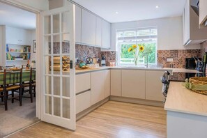 A modern kitchen with white cabinets, a wooden countertop, and a window with a view of greenery. - Little Buckley Peaceful Family Retreat Nr Sidmouth (Sidbury)