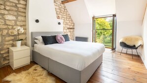 Een slaapkamer met een stenen muur, een bed met wit beddengoed, een zacht tapijt en een fauteuil met een bont plaid.