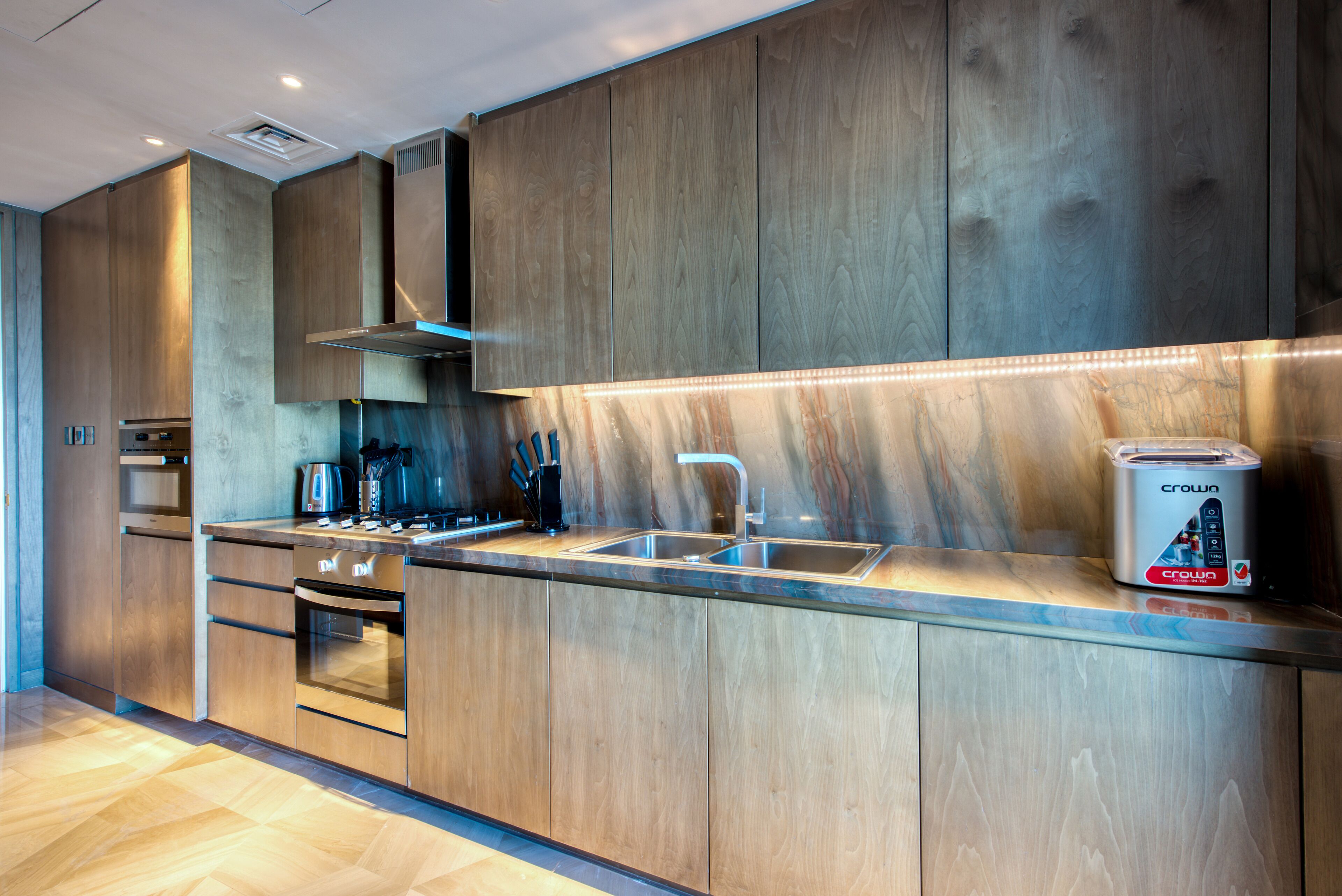 Eine moderne Küche mit Holzschränken, Edelstahlgeräten und einem eingebauten Backofen.