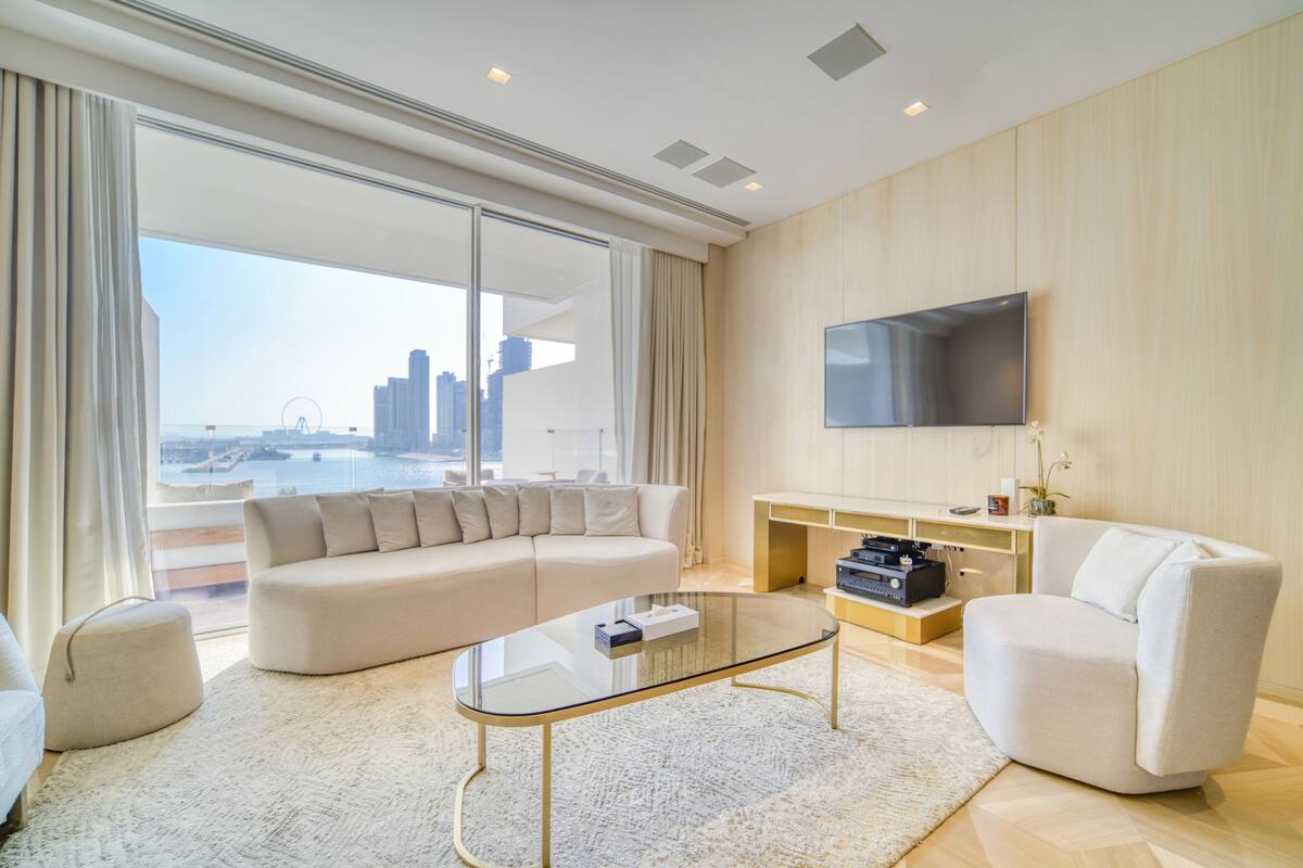 A modern living room with a large sofa, a glass coffee table, and a flat-screen TV mounted on the wall.