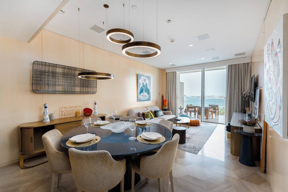A modern dining area with a round table, wicker chairs, and pendant lighting.
