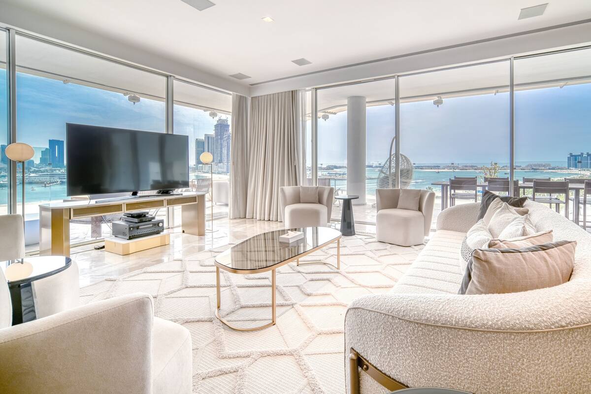 A modern living room with a large TV, comfortable seating, and a view of the city and water.