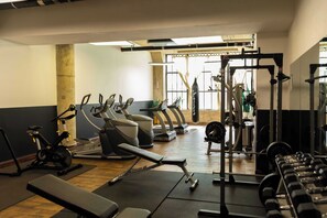 Une salle de sport équipée de matériel d’exercice, d’un banc et d’une fenêtre avec des rideaux.