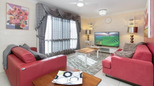 Ein Wohnzimmer mit roten Sofas, einem Couchtisch, einem Fernseher und einem Deckenventilator.