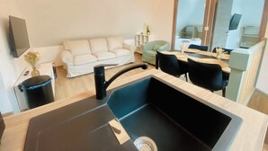 A modern kitchen with a black sink, a dining area with a table and chairs, a white sofa, and a small side table with a vase.