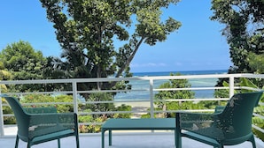 Ein Balkon mit zwei grünen Stühlen und einem Tisch, mit Blick auf einen Strand und den Ozean.