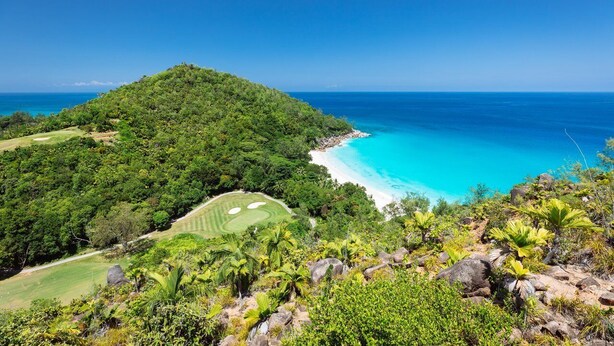 Üppige grüne Landschaft mit blauem Himmel, Strand und Golfplatz.