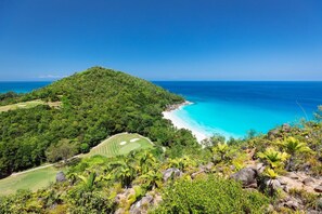 A lush green landscape with a clear blue sky, a beach, and a golf course.
