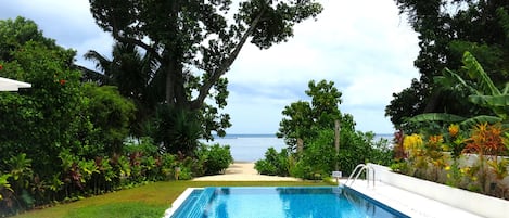 A swimming pool with a view of the ocean, surrounded by lush greenery and trees.