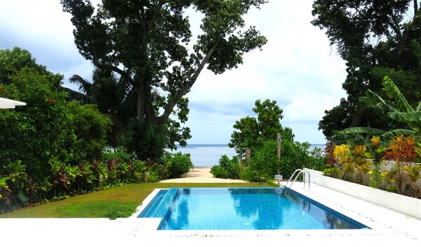 A swimming pool with a view of the ocean, surrounded by lush greenery and trees.